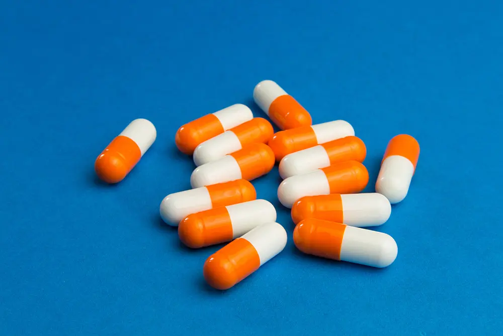 A group of orange and white capsules scattered on a blue surface.