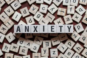 Wooden letter tiles scattered on a table. The word ANXIETY is prominently spelled out in the center using these tiles.